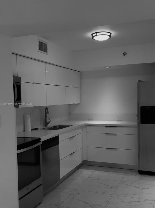 Kitchen featuring glossy flat-panel cabinetry, light-toned stone-finish countertops, stainless steel appliances, stone-finish tile flooring, and flush-mount ceiling lighting