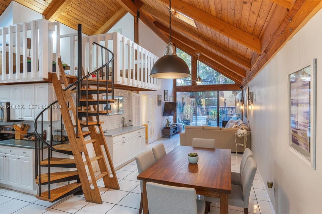 Vaulted wood-paneled ceilings, floor-to-ceiling glass paneling, white built-in cabinetry, custom metal and wood-finished spiral staircase, and lofted upper level