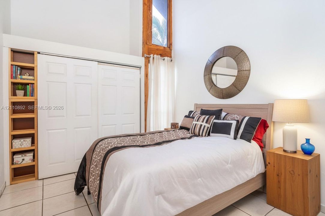 Vaulted ceilings with natural wood-trimmed vertical window, floor-to-ceiling built-in shelving, white paneled sliding closet doors, and ceramic tile flooring