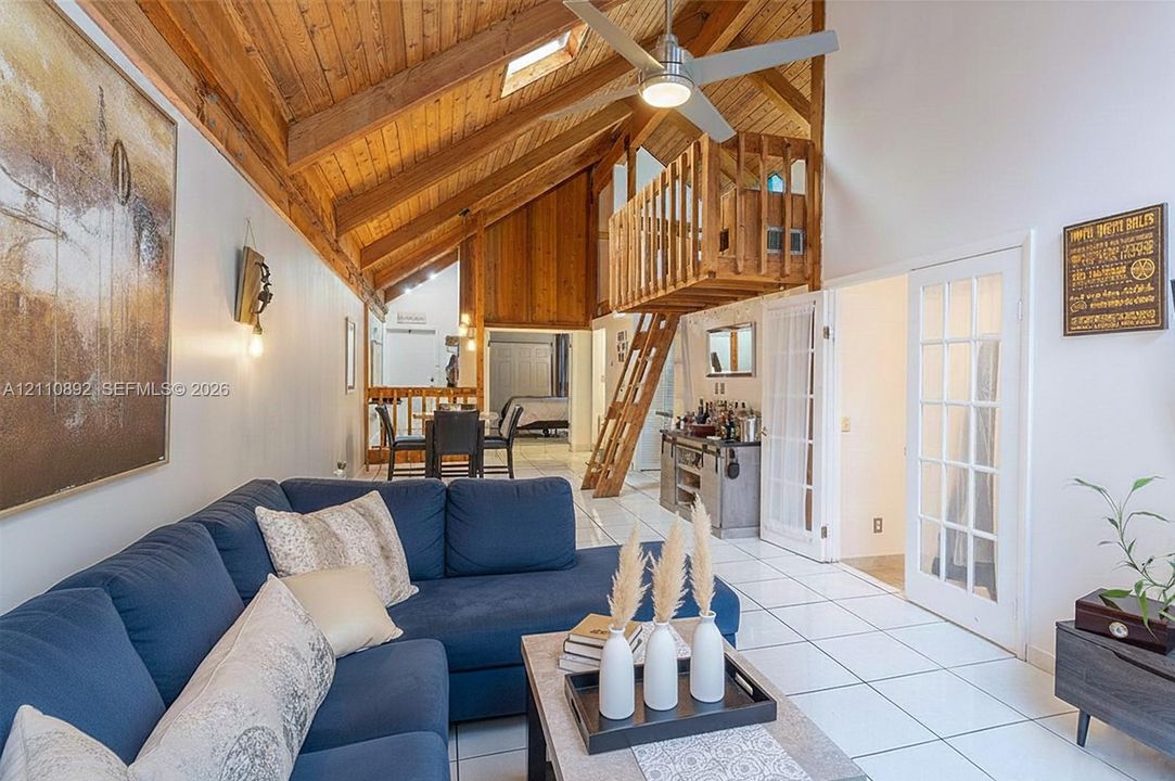 Vaulted timber-plank ceiling featuring exposed beams, skylight, wooden loft structure with integrated ladder, tile flooring, and French doors with glass panes