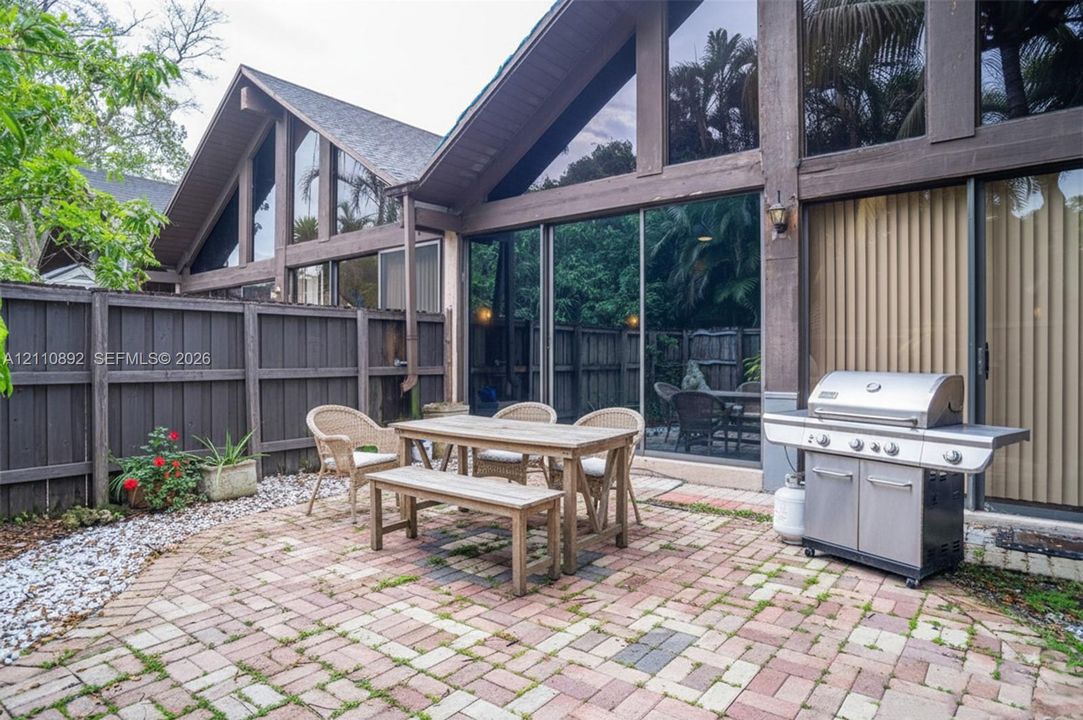 Paved brick patio featuring floor-to-ceiling glass paneling, A-frame architectural design, exterior wood-beam framing, and a perimeter wood fence