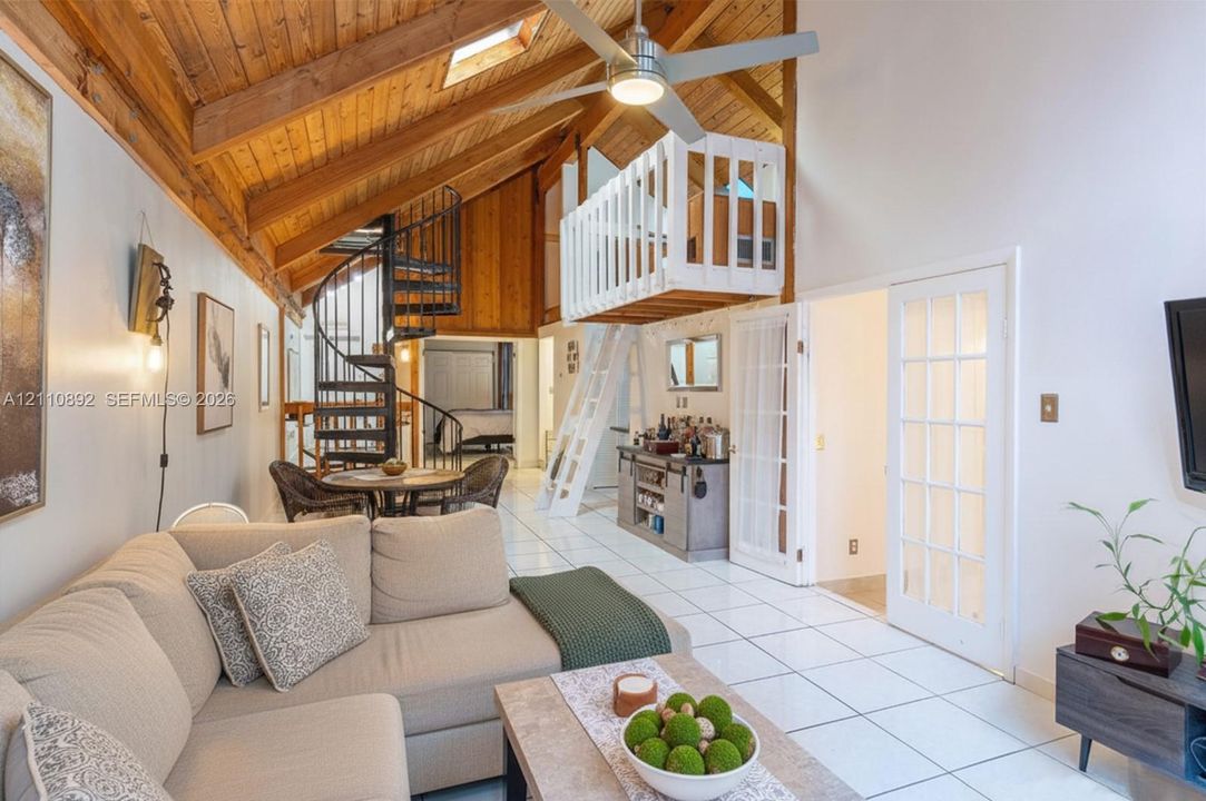 Vaulted wood-paneled ceiling with skylight, exposed wooden beams, metal spiral staircase, white-railed loft level, and French doors with glass panes