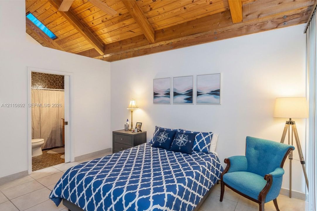 Vaulted wood-plank ceiling with exposed beams, skylight, and large-format tile flooring
