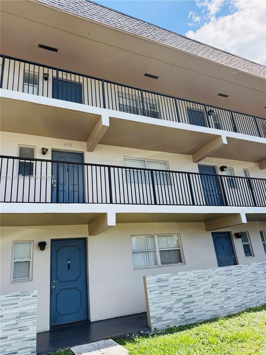 Multi-level exterior featuring black metal balcony railings, textured stone veneer privacy walls, and blue entry doors
