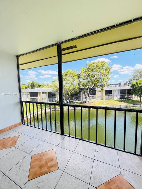Covered balcony featuring screen enclosure, metal railing, tile flooring with decorative wood-finish accents, and water frontage