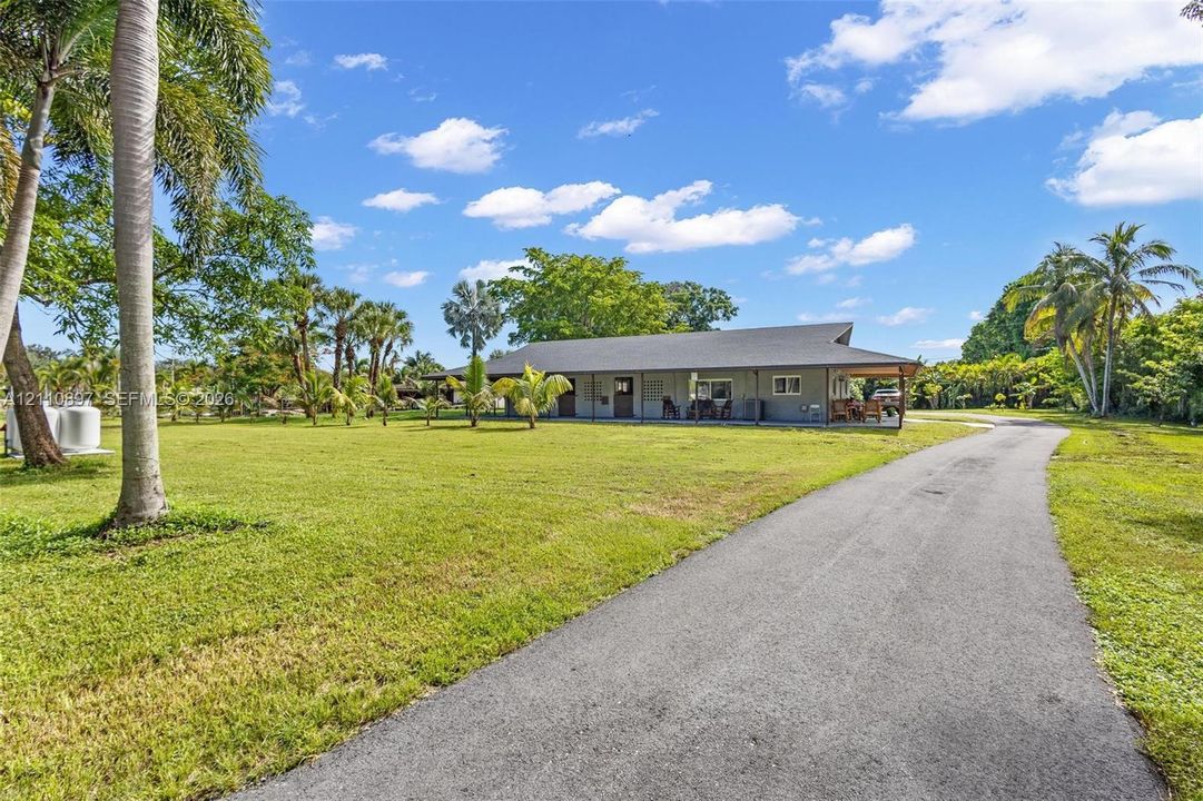 Single-story residence featuring a covered front porch, asphalt driveway, and expansive lawn with mature palm trees