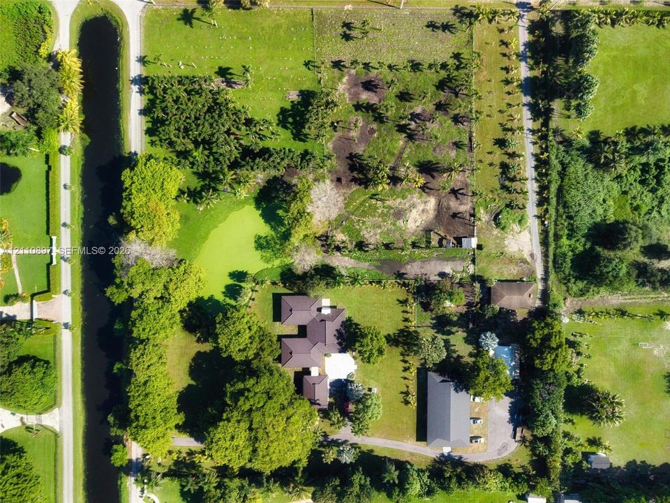 Aerial perspective of a sprawling property featuring extensive acreage, mature landscaping, a private water feature, an attached garage, and a dedicated pool area