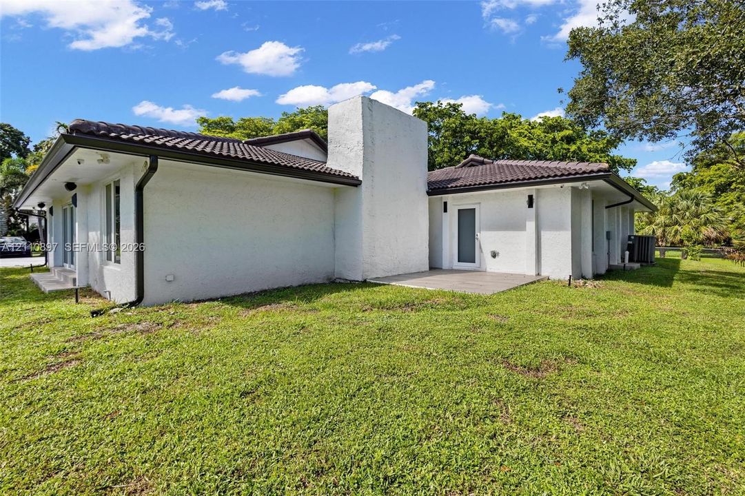Single-story exterior featuring white stucco siding, a prominent masonry chimney, dark-tiled roof, and concrete patio
