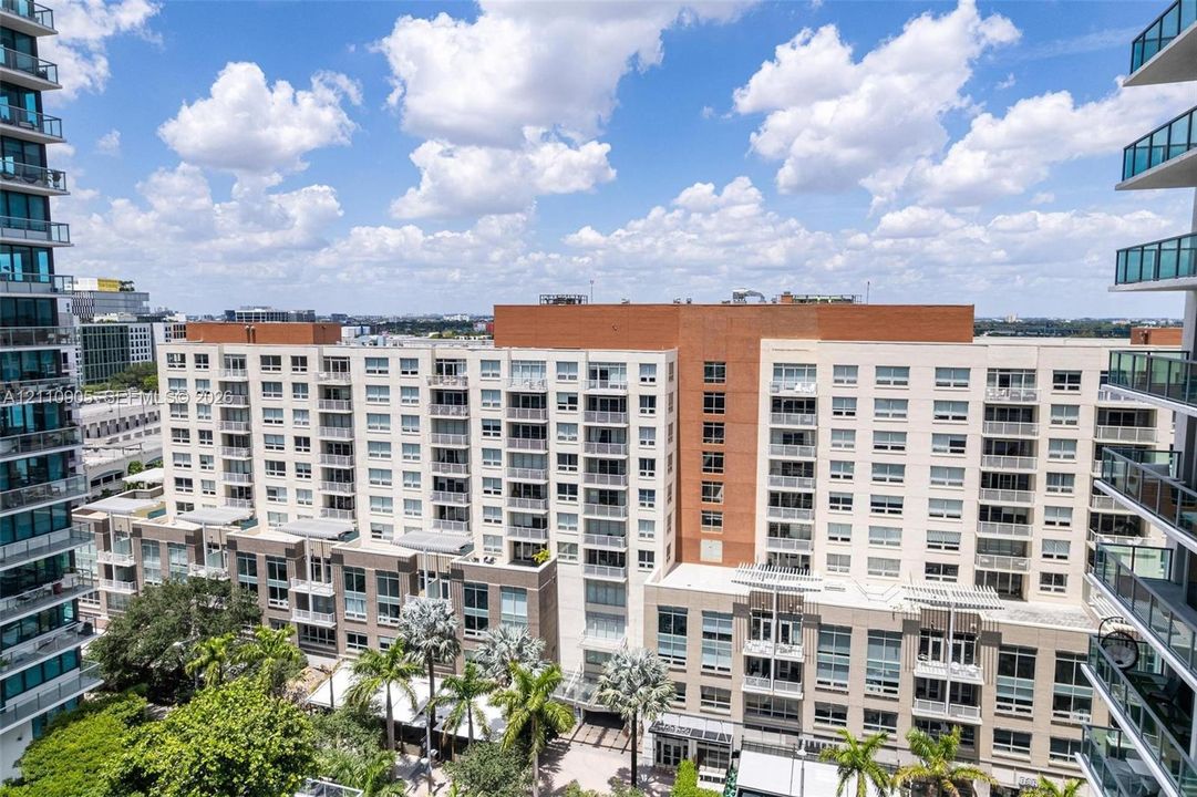 Mid-rise residential building featuring stacked balconies, brick masonry exterior, multi-pane glazing, and integrated palm tree landscaping