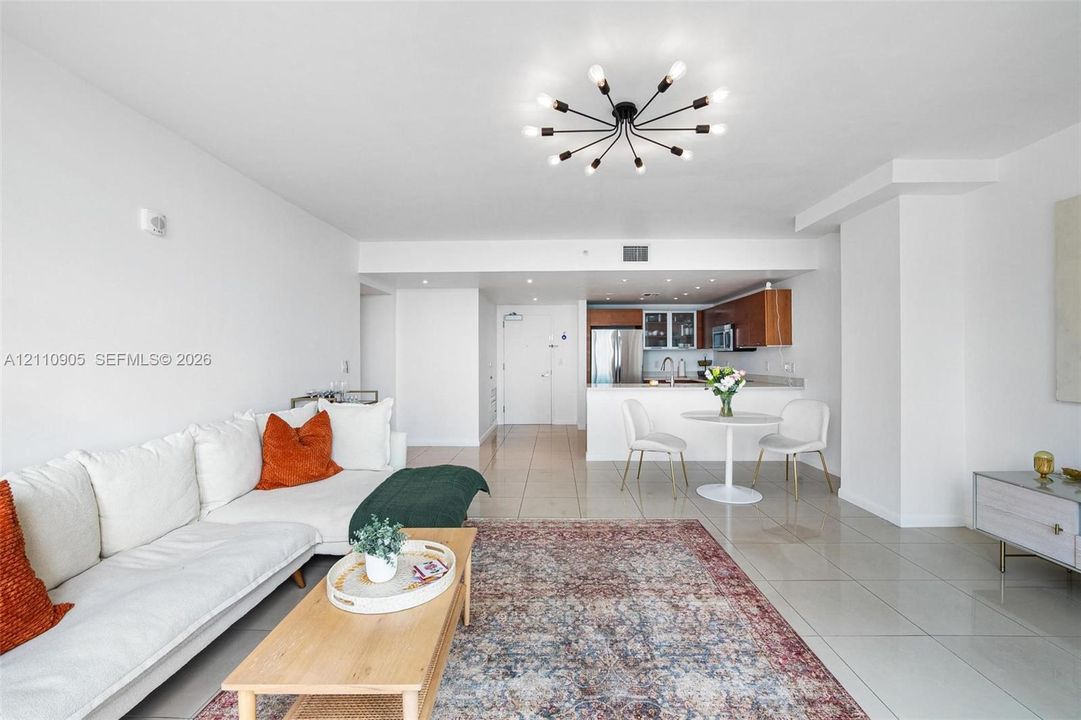 Open-concept interior featuring large-format tile flooring, a multi-arm sputnik-style ceiling light fixture, recessed lighting, and kitchen cabinetry with a wood finish