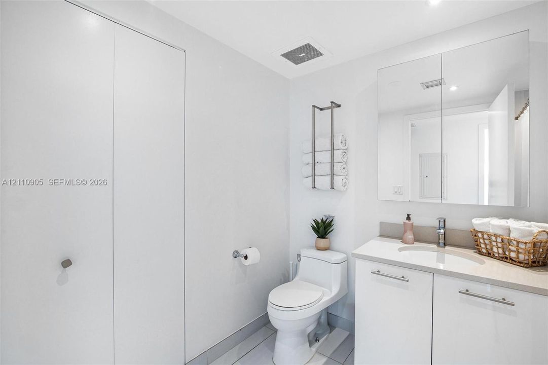Bathroom featuring a white vanity with an integrated sink, neutral stone-composite countertop, wall-mounted mirrored medicine cabinet, floor-to-ceiling storage cabinetry, and tile flooring