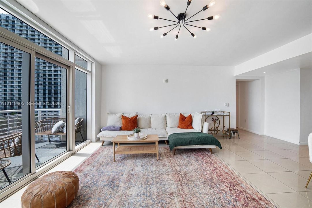 Floor-to-ceiling glass sliding doors, polished tile flooring, contemporary multi-arm spider chandelier, and a private balcony with metal railing