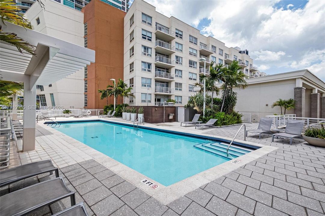 Swimming pool featuring a rectangular design, stone paver decking, integrated metal handrails, and a pergola-covered patio area
