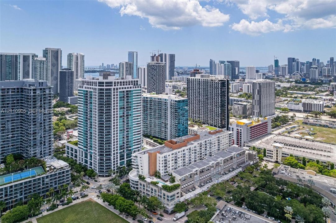 Aerial perspective of a high-rise residential building featuring floor-to-ceiling glass windows, multiple balconies, a rooftop pool terrace, and extensive urban surroundings