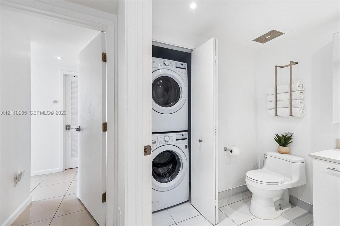 Stacked front-loading washer and dryer, one-piece dual-flush toilet, and light-toned tile flooring