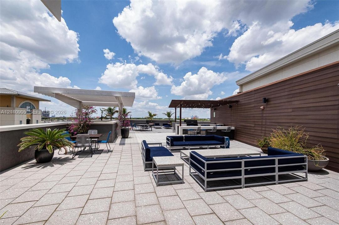 Rooftop terrace featuring concrete paver flooring, a built-in outdoor kitchen with stone-finish cabinetry, a covered pergola, and horizontal wood-style siding