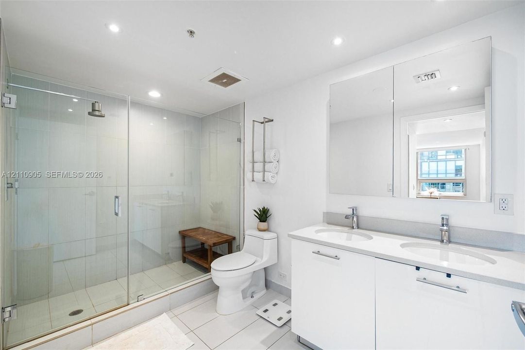 Glass-enclosed walk-in shower with tile surround, double-sink vanity with white cabinetry, quartz countertop, and large wall-mounted mirrored medicine cabinet