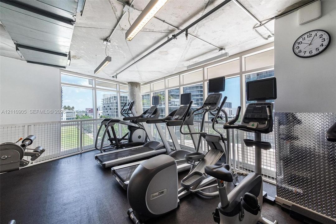 Fitness space featuring industrial-style exposed ceiling, full-height windows, rubberized flooring, and diamond-plate metal wall accents