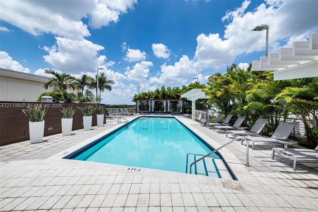 Rectangular swimming pool featuring a tiled deck, built-in pergola, privacy wall, and integrated landscaping