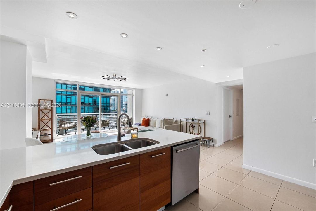 Kitchen featuring flat-panel wood-finish cabinetry, white countertops, stainless steel undermount dual-basin sink with pull-down faucet, stainless steel dishwasher, and polished tile flooring