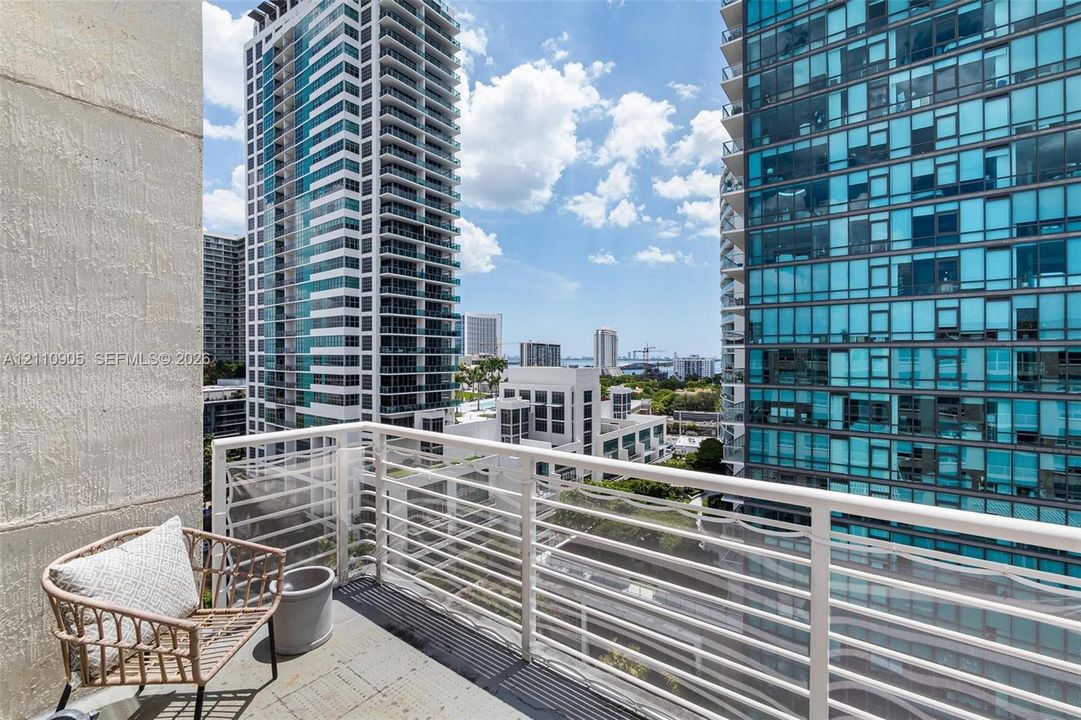 Private balcony featuring white metal railings and concrete flooring, overlooking high-rise structures and urban skyline