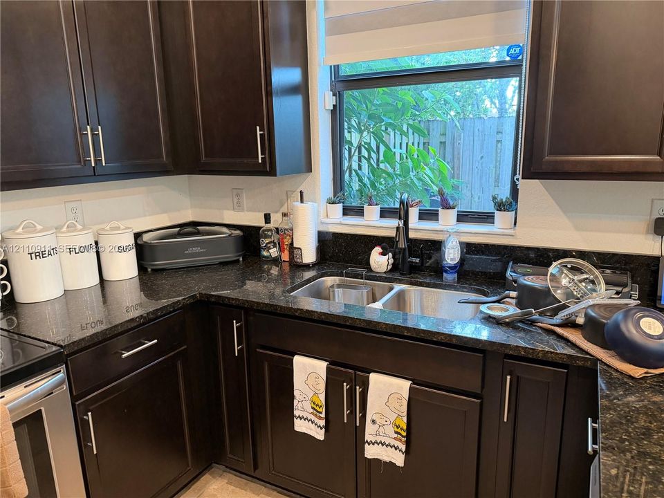 Dark finish cabinetry, dual-basin stainless steel sink, stone countertop, matte black faucet, and window with natural light
