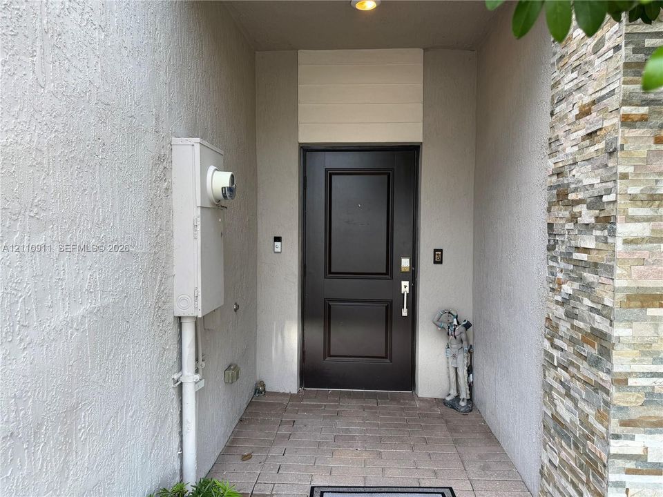Covered entryway featuring a solid-panel door, stacked stone veneer siding, and paver flooring