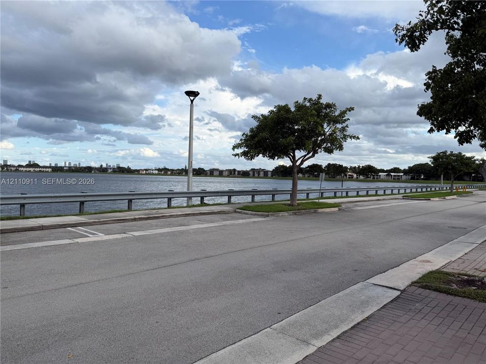 Waterfront location featuring a paved roadway, concrete curbing, mature trees, and metal guardrail