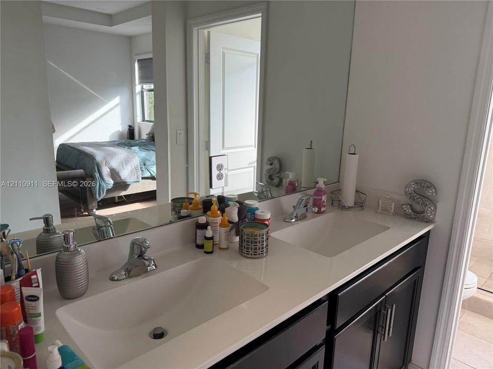 Dual-sink vanity featuring a light-toned solid surface countertop, rectangular undermount basins, dark-finished cabinetry with metallic hardware, and a full-width wall mirror