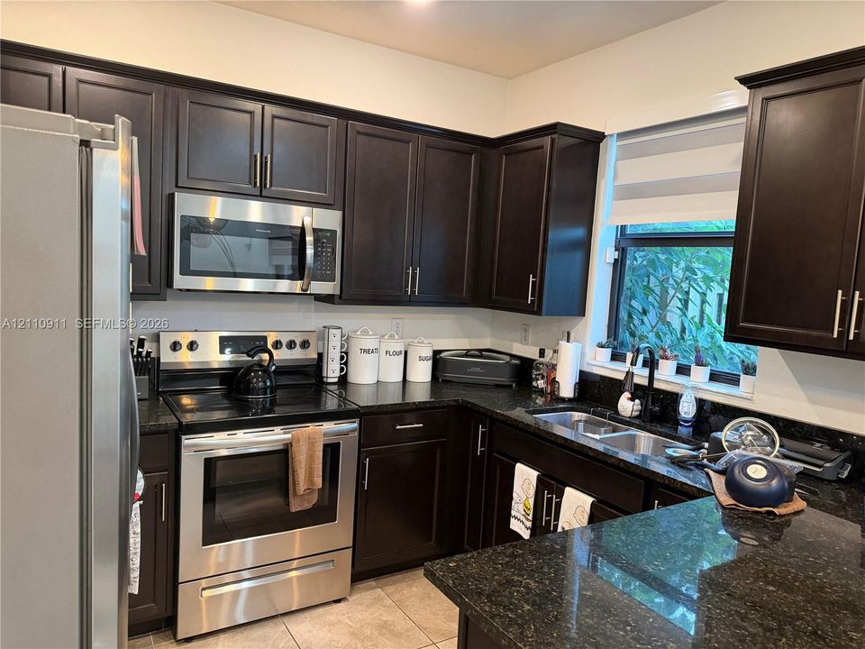 Kitchen featuring dark-finish cabinetry, stainless steel appliances, dual-basin sink, and stone-surface countertops
