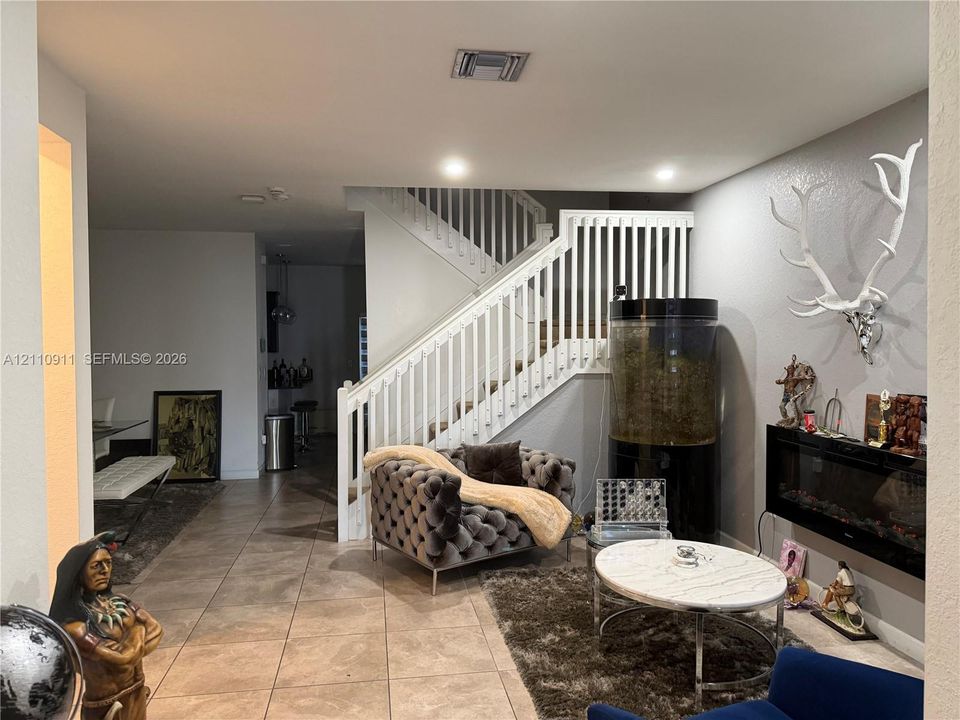 Open-concept interior featuring large-format ceramic tile flooring, white-painted wooden staircase railing, and a built-in horizontal electric fireplace