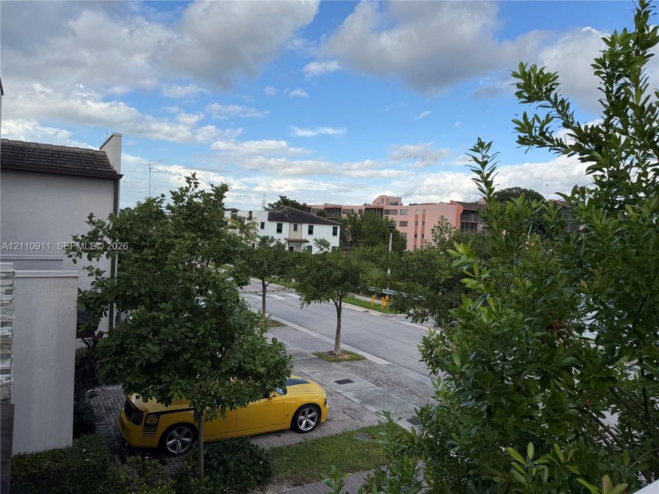 Street-level perspective featuring paved sidewalk, mature landscaping, and multi-story structural exterior