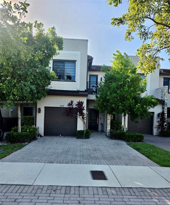 Contemporary exterior featuring stucco siding, stone veneer accents, a paved driveway, and an attached garage