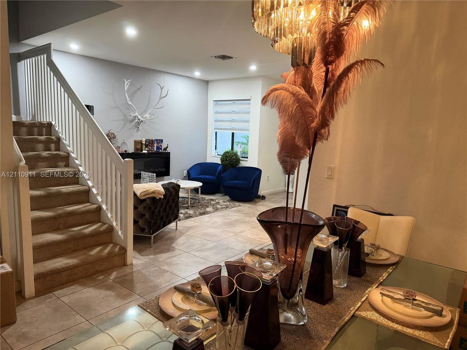Open-concept interior featuring large-format floor tiling, a white wooden staircase railing, recessed lighting, and a wall-mounted electric fireplace