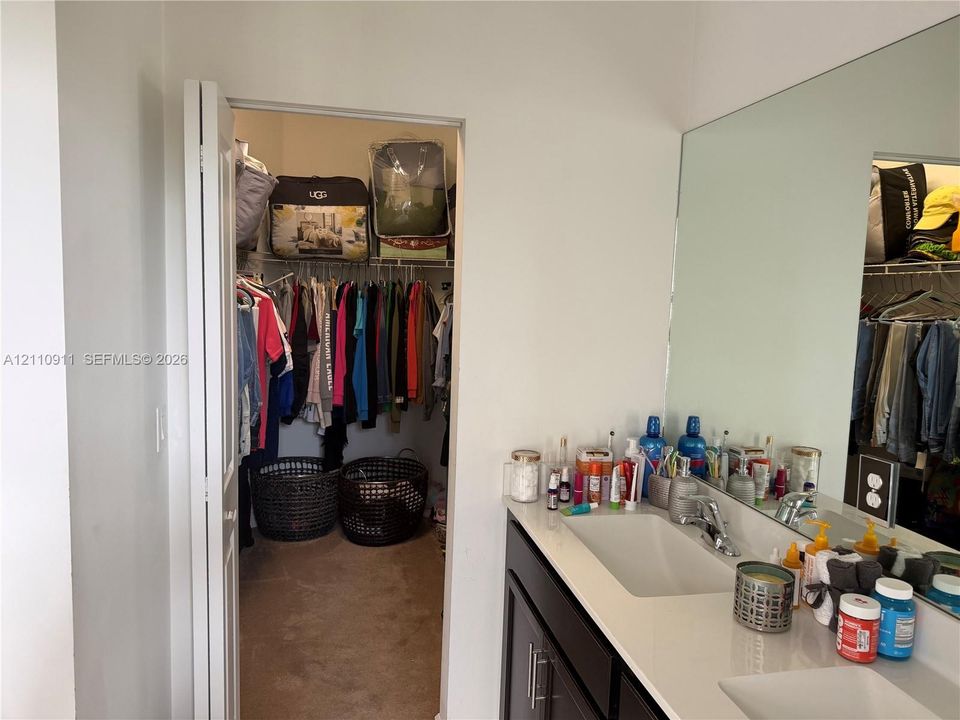 Vanity with dual integrated rectangular sinks, stone-finish countertop, dark cabinetry, and full-width wall mirror, featuring a walk-in closet with built-in shelving