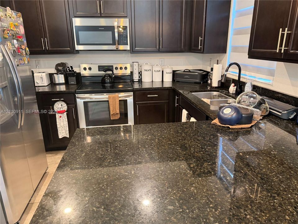 Kitchen featuring dark wood cabinetry, stainless steel appliances, speckled stone countertops, and a matte black gooseneck faucet