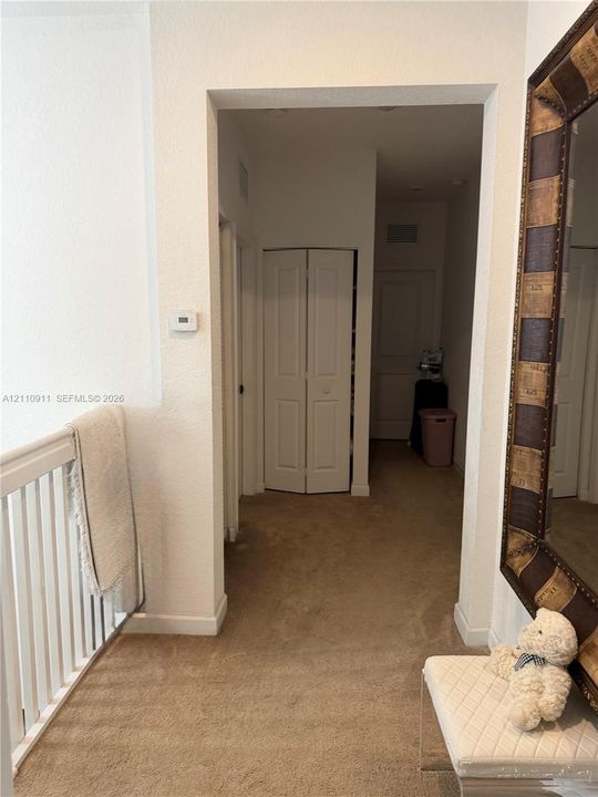 Interior hallway featuring neutral carpeting, a white-paneled bi-fold closet door, and a white balustrade railing