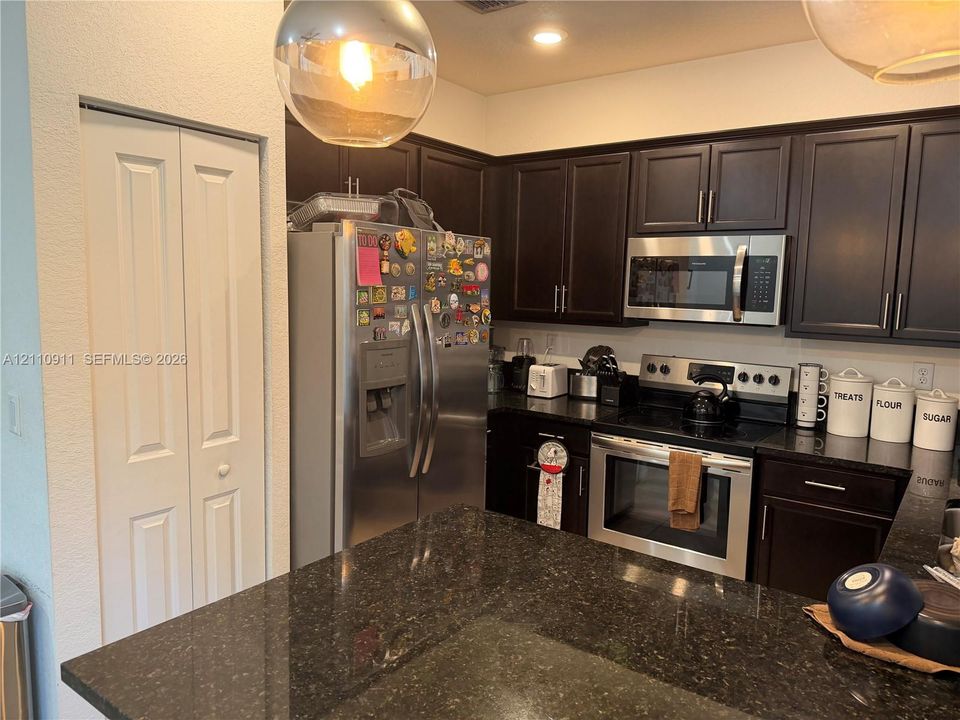 Kitchen featuring dark-finish cabinetry, stone-surface countertops, stainless steel appliances, and pendant lighting