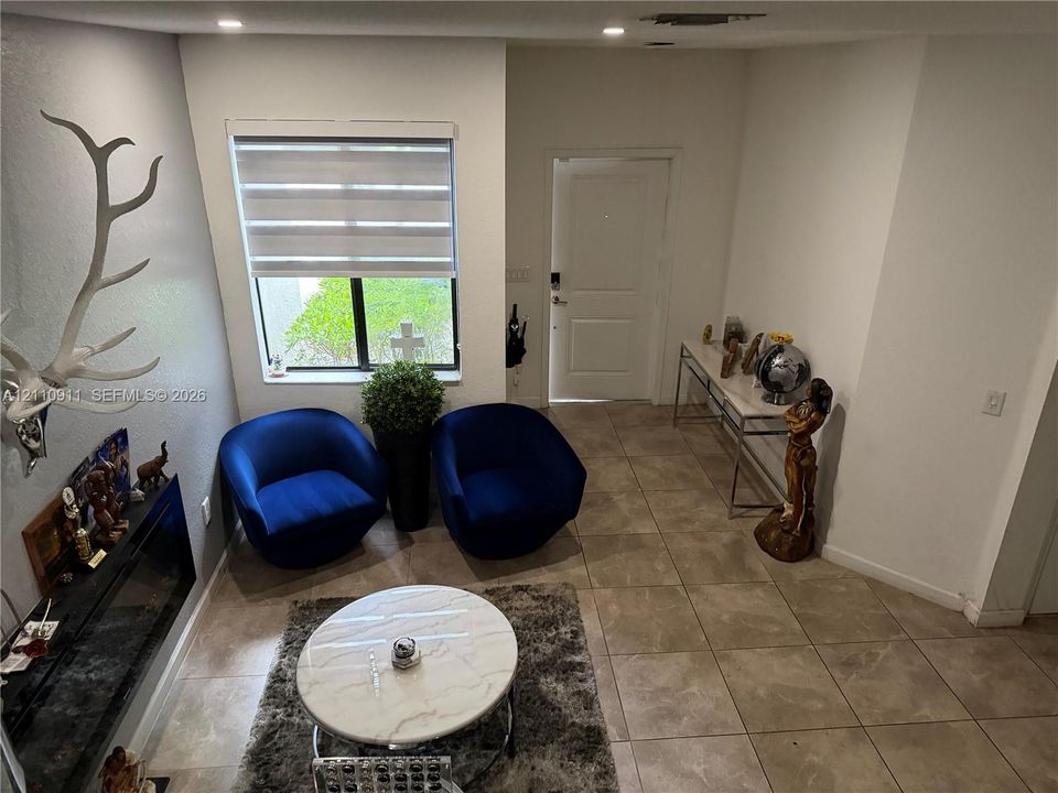 Entryway featuring large-format ceramic tile flooring, a wall-mounted electric fireplace, recessed ceiling lighting, and a window with motorized dual-layer shade