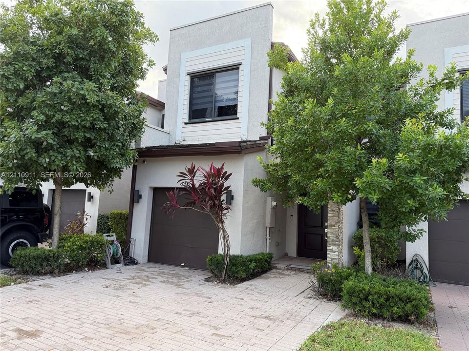 Contemporary two-story exterior featuring light-toned stucco siding, a paver driveway, an attached garage, and stone veneer accents