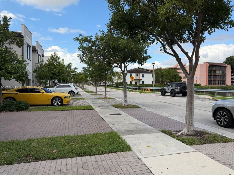 Streetscape featuring paved brick driveways, concrete sidewalks, and mature canopy trees