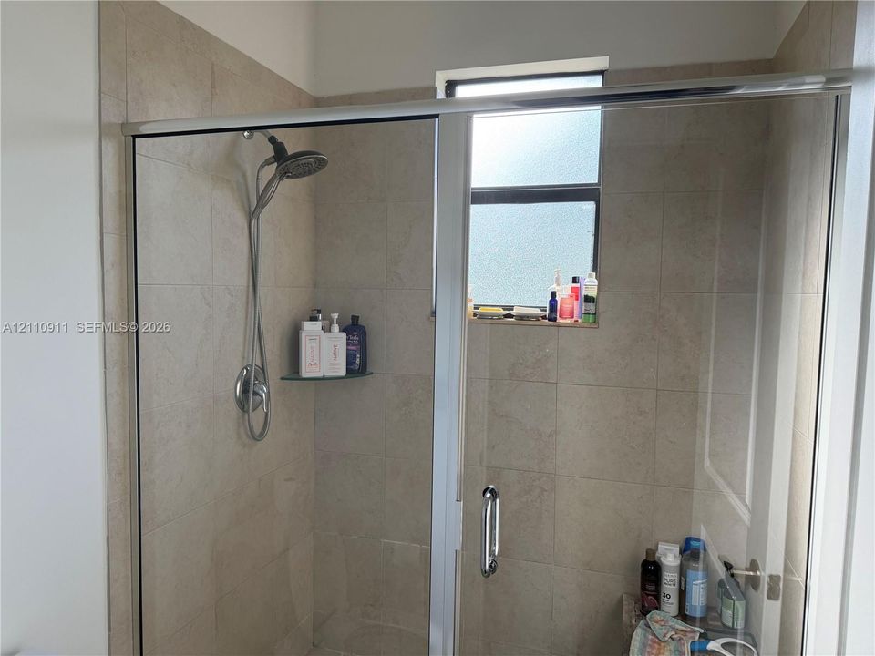 Walk-in shower enclosure featuring floor-to-ceiling tile, a chrome sliding door system, a multi-function shower head, and an integrated window