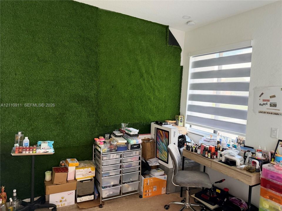 Interior space featuring a textured artificial turf wall accent and dual-layered horizontal privacy blinds