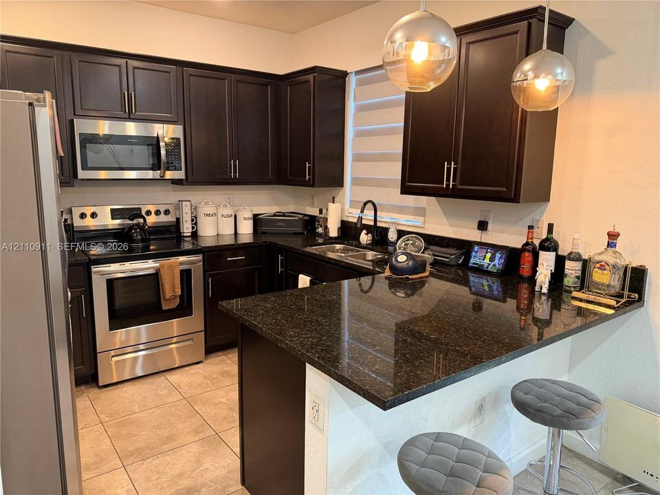Kitchen featuring dark-finish cabinetry, stone countertops, stainless steel appliances, tile flooring, and glass pendant lighting