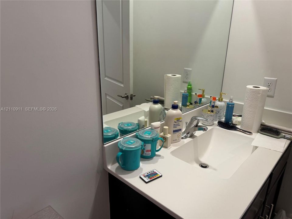 Single-sink vanity featuring a white solid-surface countertop, an integrated rectangular basin, a chrome faucet, and a large-format frameless mirror