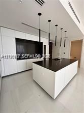 Modern kitchen featuring white flat-panel cabinetry, a central island with a dark countertop, recessed lighting, and a series of minimalist pendant lights
