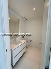 Wall-mounted white vanity with a rectangular integrated sink, stone countertop, large-format tile flooring, and a full-height backlit mirror