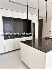 Modern kitchen featuring white flat-panel cabinetry, dark stone countertops, a built-in wine refrigerator, and cylindrical pendant lighting