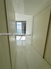 Hallway featuring large-format light-toned flooring, minimalist door frames, and floor-to-ceiling glass paneling