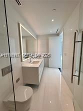 Modern bathroom featuring floor-to-ceiling tile, a floating dual-sink vanity with integrated lighting, a wall-mounted toilet, and a glass-enclosed shower